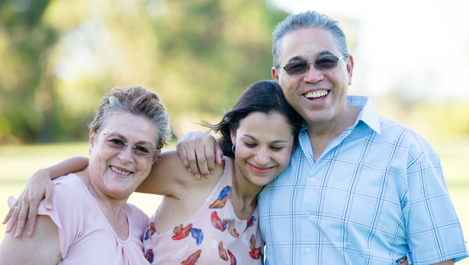 A young adult poses with her arms around her mother and father.