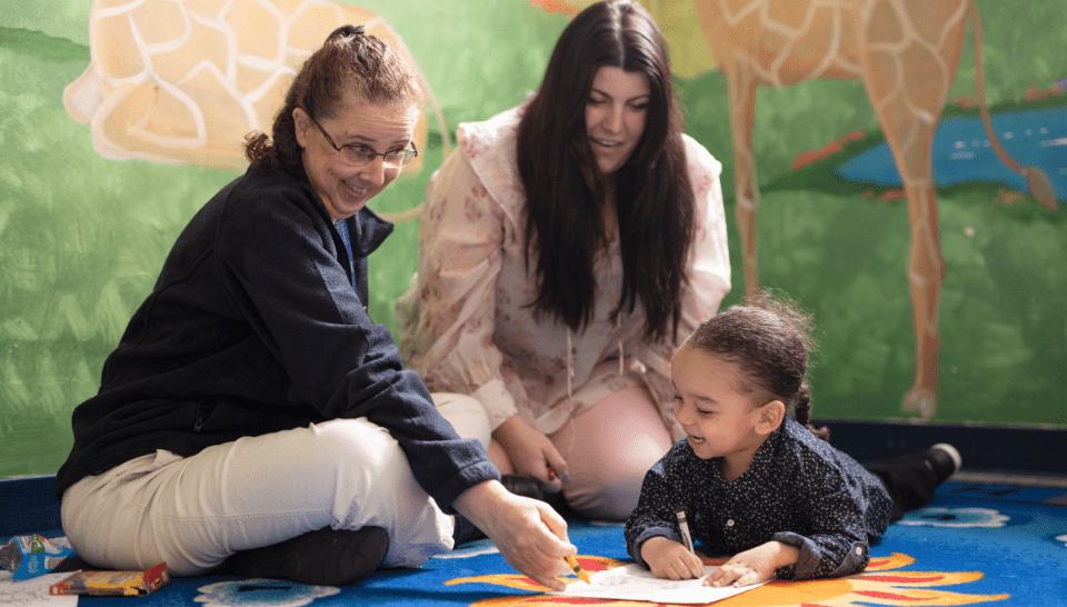 Two EI providers work with a toddler girl on a floor mat.