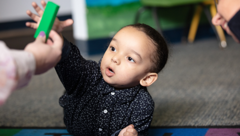 A toddler girl takes a green block from an early intervention provider.