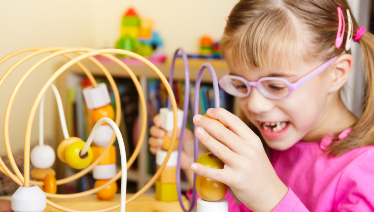 A child with visual impairments play with wooden beads on an educational roller coaster toy.