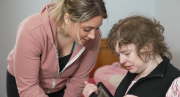 Two women; one is looking at an iPad.