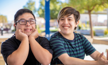 Two adult individuals with developmental disabilities sit at a picnic table.
