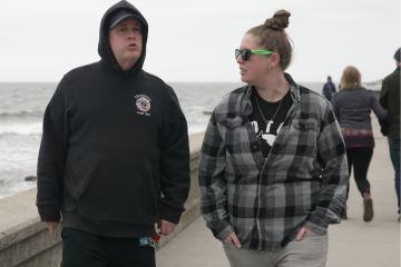 Two people walk along the sea wall at the beach.