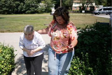 A woman assists another woman on a walk.