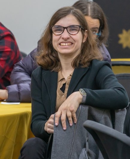 Sentinels member Rachel Ferreira, a young woman with medium-length brown hair and glasses, is pictured as she sits at one of the round tables and participates in the meeting.