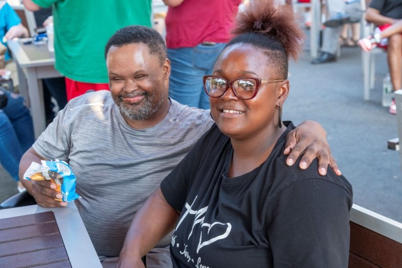 A man eating an ice cream puts his arm around a woman; both are smiling at the camera.