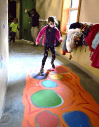 A girl wearing a pink coat follows a colorful pattern on the floor of the Roger Williams Park Zoo's sensory pathway