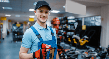 A young man working in a hardware store holds a pneumatic nailer.