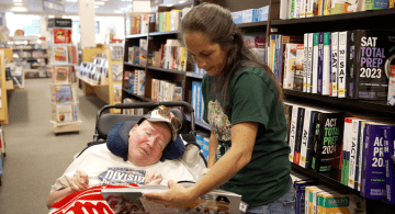 An individual in a wheelchair looks at an NBA 75 book with a direct support professionalore