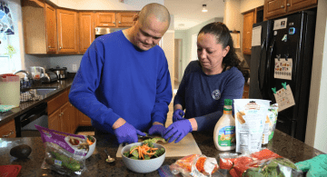 Two people prepare a salad in a kitchen.