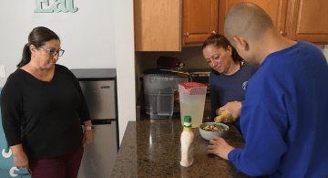 Two people make a salad as another looks on.