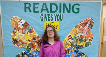 Michaela Davin stands in front of butterfly wings on a wall that says Reading Gives You Wings.