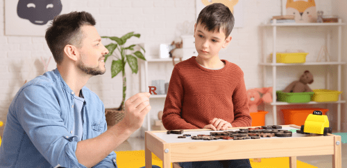 A young man who is a professional in the disability field works with a child who has autism in an office setting.