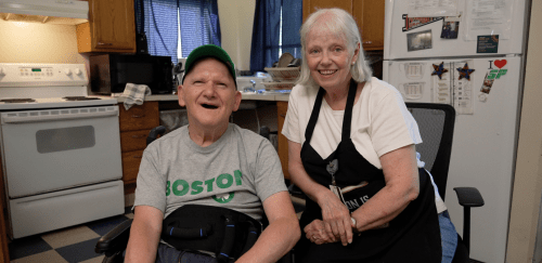 A Direct Support Professional sits with a man in a kitchen.