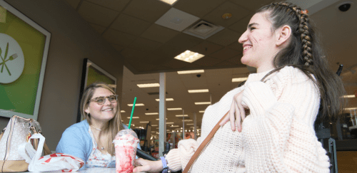 Two people smile as they sit in a coffee shop.