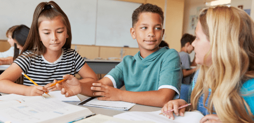 Three elementary school children work together at a table in a classroom.