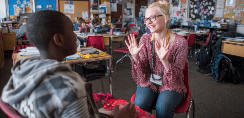 A teacher interacts with a student in a classroom.