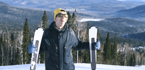 A person stands on a mountain holding a pair of skis.