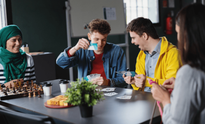 A group of individuals, including a person with a developmental disability, play cards and games at a table.