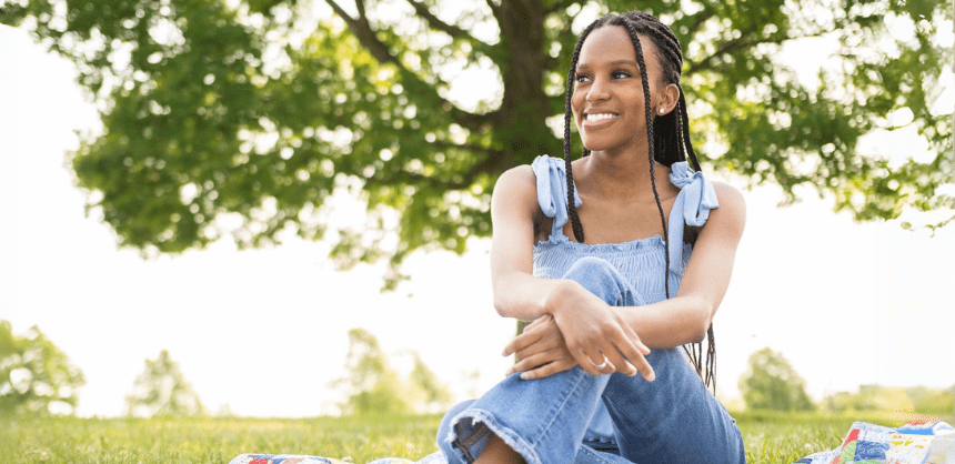 A young woman sits on blanket in a park setting.