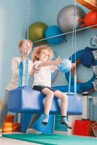 A boy receives therapy on a swing with a sensory ball